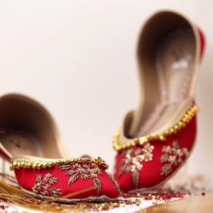 May include: A pair of red embroidered flat shoes with gold embellishments. The shoes have a pointed toe and are decorated with floral patterns.