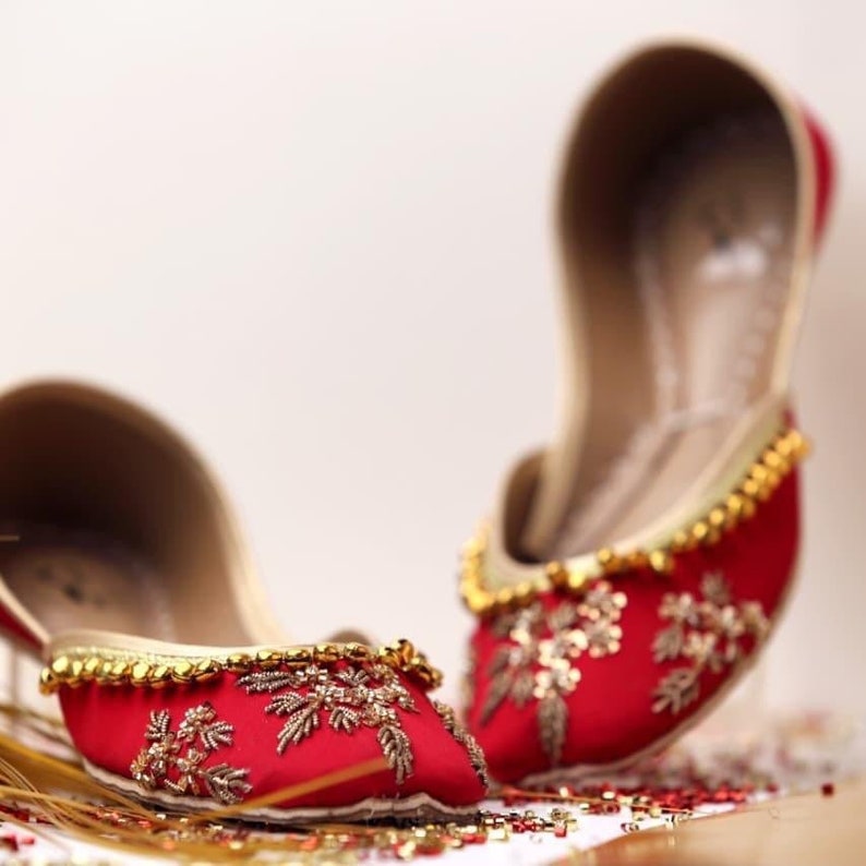 May include: A pair of red embroidered flat shoes with gold embellishments. The shoes have a pointed toe and are decorated with floral patterns.