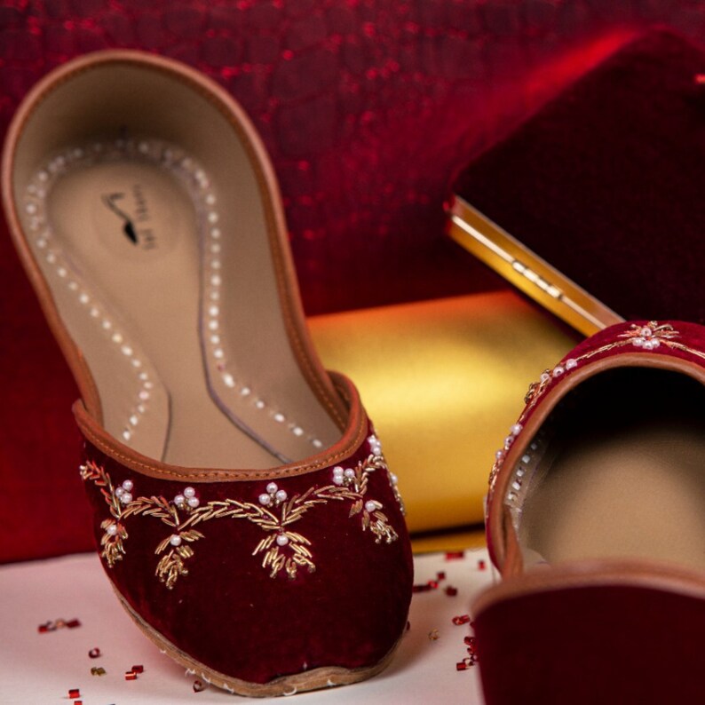 May include: A pair of maroon velvet shoes with gold embroidery and pearl accents. The shoes have a pointed toe and a low heel.