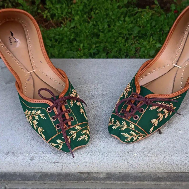 May include: A pair of green embroidered flat shoes with brown laces. The shoes have a pointed toe and are decorated with gold embroidery of leaves.