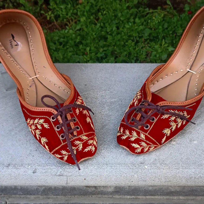 May include: A pair of red velvet shoes with gold embroidery and brown laces. The shoes have a pointed toe and a flat heel.