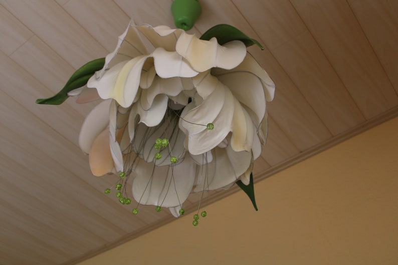Może przedstawiać: Biała lampa sufitowa w kształcie kwiatu z zielonymi akcentami. Lampa wykonana jest z tkaniny i ma delikatny, kobiecy design.