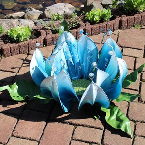 Pode incluir: Uma escultura de flor de metal azul e branco com folhas verdes. A escultura &eacute; feita de muitas pe&ccedil;as individuais de metal que s&atilde;o unidas para formar a flor.