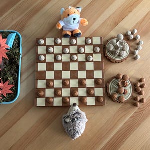 May include: A brown and beige checkerboard game with brown acorn pieces. There are two wooden acorn trees with brown acorns on them. A brown and white fox plush toy and a brown hedgehog plush toy are on the board.