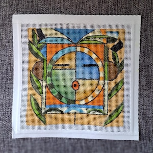 Może przedstawiać: Kolorowy, geometryczny wzór haftu igłą przedstawiający stylizowaną twarz w kwadratowej ramie. Twarz podzielona jest na sekcje w kolorze pomarańczowym, niebieskim, zielonym i żółtym. Gałązki oliwne i brązowe oliwki otaczają twarz, wszystko na beżowym tle.