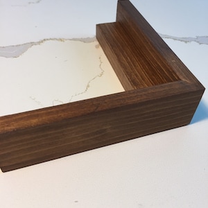 May include: A close-up of a corner of a wooden frame. The frame is a rich brown color and has a smooth finish.
