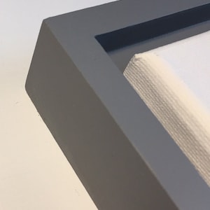 May include: A close-up of the corner of a gray picture frame with a white canvas inside.