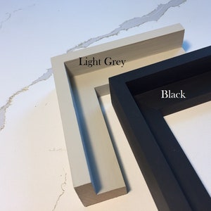 May include: Two wooden picture frames, one light grey and one black, are displayed against a white background. The light grey frame is labeled "Light Grey" and the black frame is labeled "Black". The frames are shown at an angle, highlighting their depth and construction.
