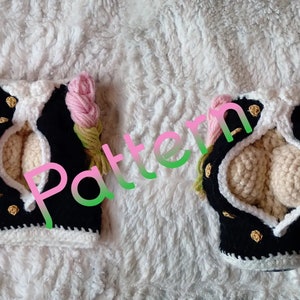 May include: A crocheted black and white vest with gold buttons and pink and green flower accents. The vest has a large opening in the front.