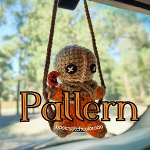 May include: Crocheted Sam doll hanging from a brown string, with a pumpkin lollipop. The doll has black cross-shaped eyes and a tan head. The word "Pattern" is in orange letters. The background is a blurred view of trees.