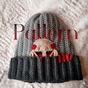 Puede incluir: Un gorro tejido gris y negro con un diseño de criatura beige y detalles rojos. La palabra "Pattern" se muestra en rojo sobre el gorro. El gorro está hecho de un hilo suave y texturizado.