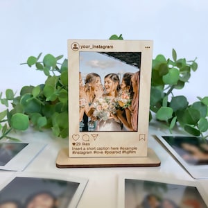 May include: A wooden Instagram photo frame with a picture of a group of women smiling. The frame has a heart, comment, direct message, and save icon. The text "29 likes" and "Insert a short caption here #example #instagram #love #polaroid #fujifilm" is below the picture.