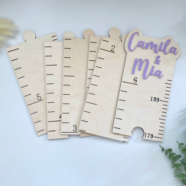 Pode incluir: Gr&aacute;fico de crescimento de madeira com uma inscri&ccedil;&atilde;o roxa que diz "Camila & Mia". O gr&aacute;fico tem marcas em polegadas e cent&iacute;metros.