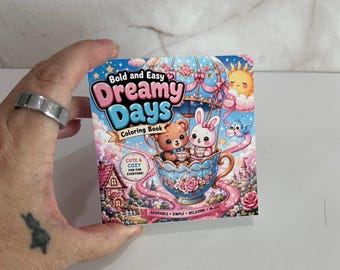 May include: A square coloring book titled Bold and Easy Dreamy Days. The cover features a brown bear and a white rabbit sitting in a floral teacup hot air balloon, surrounded by a pink path, a small house, a sun, and a blue bird in the sky.