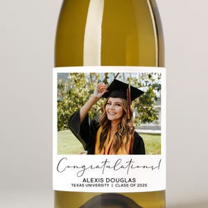 May include: A wine bottle with a personalised label celebrating graduation. The label displays a photograph of a graduate in cap and gown, with the text "Congratulations!", the graduate's name, university, and class year.