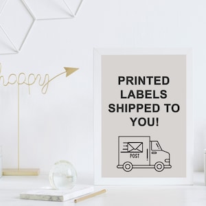 May include: A framed print with the text "PRINTED LABELS SHIPPED TO YOU!" above a black and white illustration of a delivery truck. The print is on a white desk with decorative items.