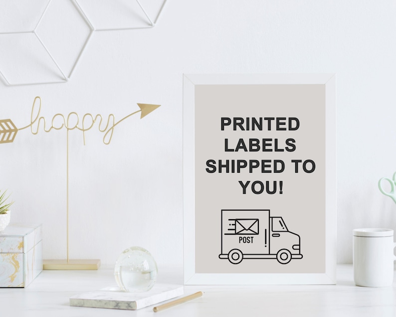 May include: A framed print with the text "PRINTED LABELS SHIPPED TO YOU!" above a black and white illustration of a delivery truck. The print is on a white desk with decorative items.