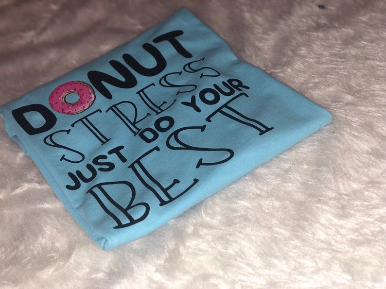 May include: Light blue t-shirt with the text "Donut stress just do your best" in black lettering. A pink and white donut graphic is above the text.