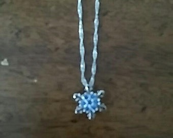 Op de afbeelding: Een zilveren ketting met een blauwe sneeuwvlok hanger.