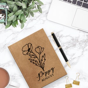 May include: A brown notebook with a black poppy flower illustration and the text "Poppy August".