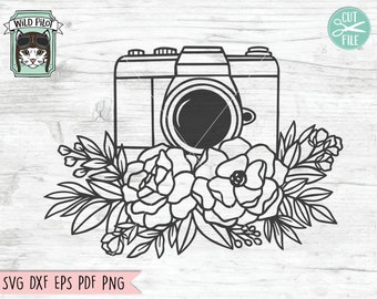 May include: Black and white line art of a camera with a floral arrangement. The design includes the text "Wild Pilot" and "Cut File". The bottom of the image includes the text "SVG DXF EPS PDF PNG".