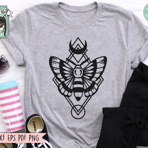 May include: A gray t-shirt with a black graphic of a moth inside a geometric shape with a crescent moon above it. The graphic is in a minimalist style.
