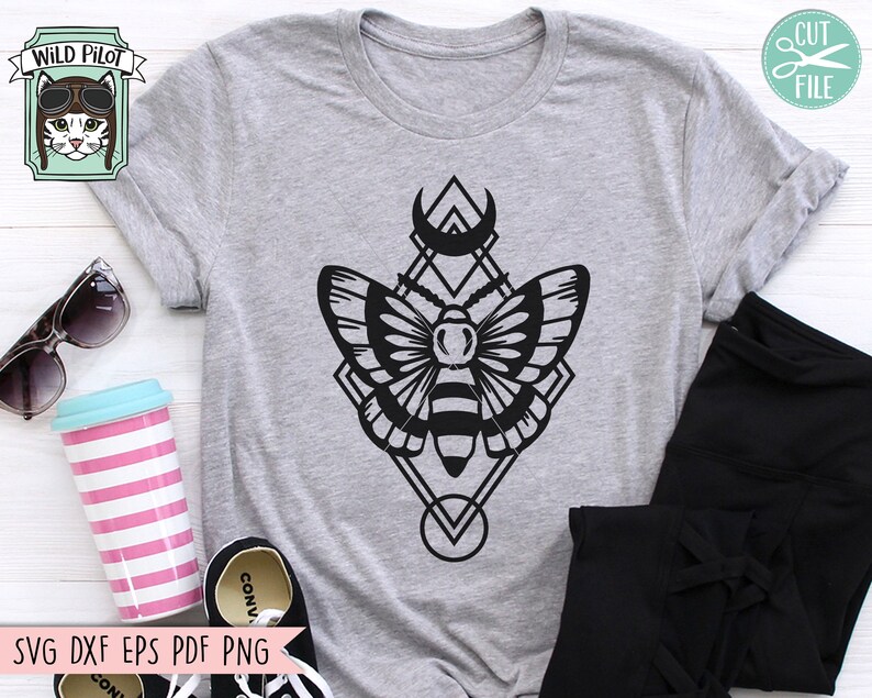May include: A gray t-shirt with a black graphic of a moth inside a geometric shape with a crescent moon above it. The graphic is in a minimalist style.