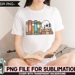 May include: A white t-shirt with a graphic of a skull resting on a stack of colorful books. The graphic is in a vintage style with a distressed look. The t-shirt is being worn by a person sitting on a bed.