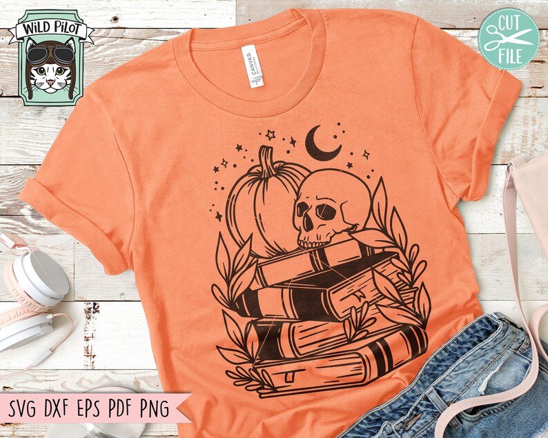 May include: Orange t-shirt with a black graphic of a skull, pumpkin, books, and crescent moon. The shirt also features the text "SVG DXF EPS PDF PNG" at the bottom. A Wild Pilot logo is in the upper left corner.