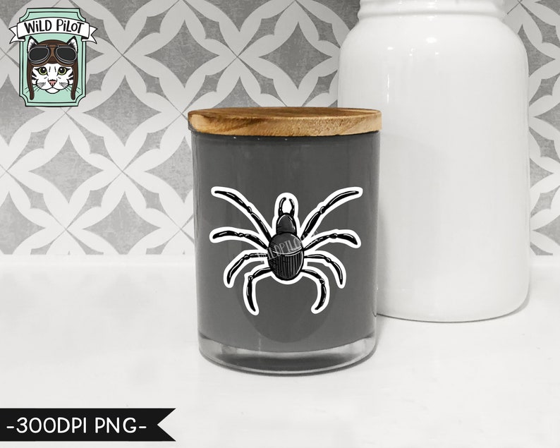 May include: A gray candle jar with a wooden lid and a black spider sticker on the front. The sticker is a simple line drawing of a spider with eight legs.