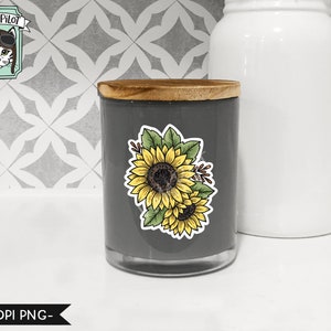 May include: A gray candle jar with a wooden lid and a sunflower decal. The decal features two sunflowers with green leaves and stems.