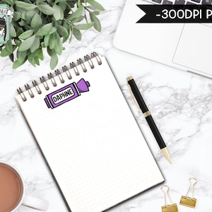 Peut inclure: Un carnet blanc avec un surligneur violet sur lequel est inscrit "Daphne". Le carnet est pos&eacute; sur une surface en marbre blanc avec un stylo noir, un ordinateur portable et une tasse de caf&eacute;.