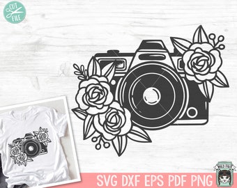 May include: Black and white illustration of a vintage camera with floral accents. The camera has a large lens and is surrounded by roses and leaves.