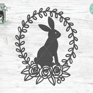 May include: A black silhouette of a rabbit sitting inside a wreath of leaves and flowers. The wreath is made of simple, stylized leaves and three roses.