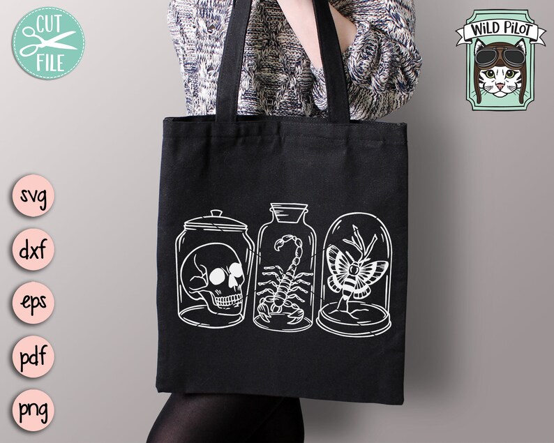 May include: A black tote bag with a white design of three glass jars containing a skull, a scorpion, and a butterfly. The text "WILD PILOT" is in a banner above the jars.