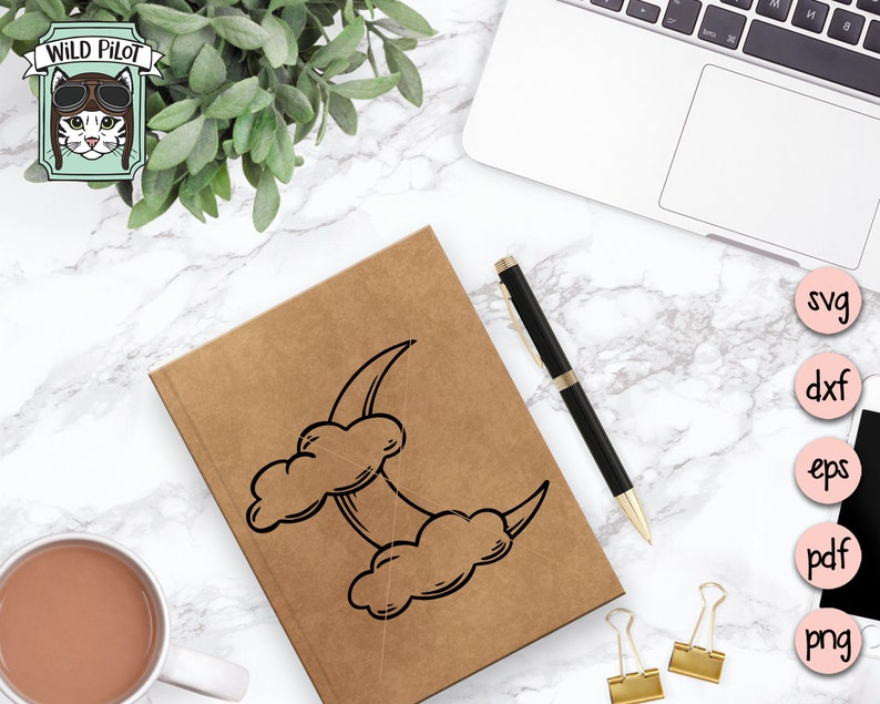May include: A brown notebook with a black and white illustration of a crescent moon and clouds. The notebook is on a white marble surface with a pen and paper clips.