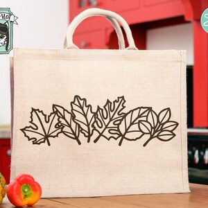 May include: A beige tote bag with a brown outline of autumn leaves printed on the front. The bag is made of burlap and has a brown leather handle.