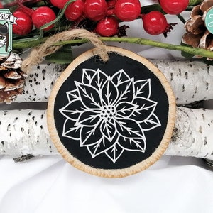 May include: A black and white poinsettia flower design on a round wooden ornament. The ornament is ideal for Christmas decorations.