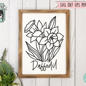 May include: A framed sign featuring a black and white line drawing of a daffodil flower. The word "Daffodil" is written in a script font below the flower. The frame is made of wood with a rustic finish. The Wild Pilot logo is in the upper left corner.