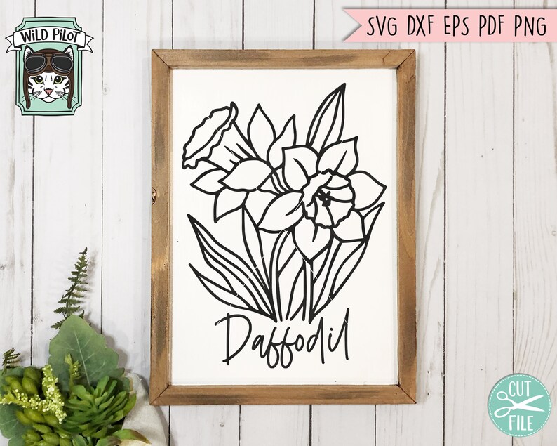 May include: A framed sign featuring a black and white line drawing of a daffodil flower. The word "Daffodil" is written in a script font below the flower. The frame is made of wood with a rustic finish. The Wild Pilot logo is in the upper left corner.