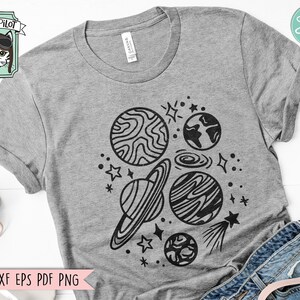 Pode incluir: Uma camiseta cinza com um design preto e branco de planetas, estrelas e um cometa. O design est&aacute; centralizado na camiseta.
