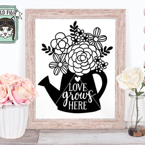 May include: Black and white silhouette of a watering can filled with flowers. The text "LOVE grows HERE" is written on the watering can.