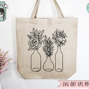 May include: A black and white line drawing of three vases with flowers. The vases are tall and slender, and the flowers are simple and elegant. The design is perfect for a tote bag or other home decor.
