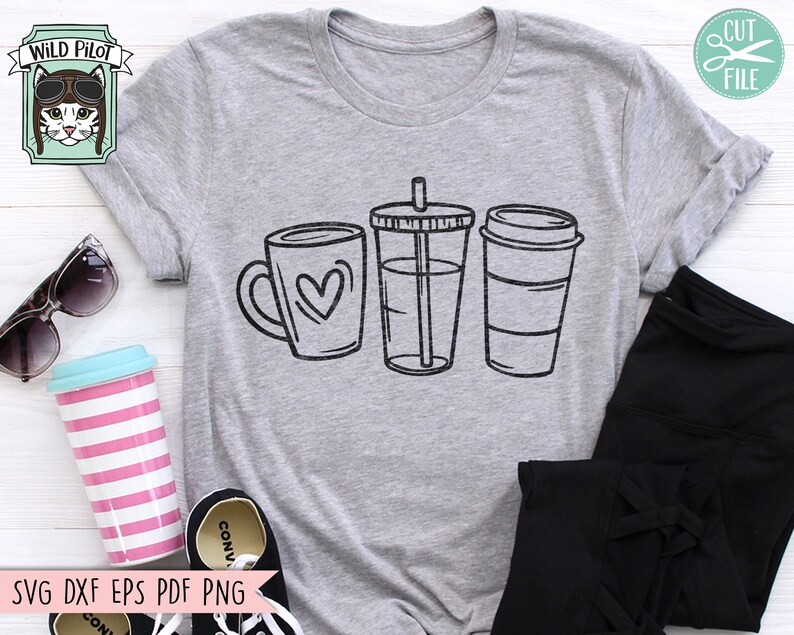 May include: A grey t-shirt featuring a design of three coffee cups. The cups are black and white and have a simple design. The design includes a mug with a heart, a tall cup with a straw, and a takeaway cup with a lid.