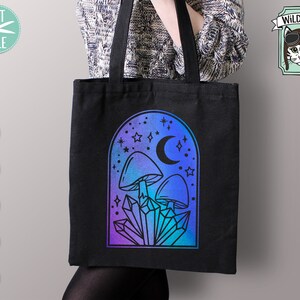 May include: A black tote bag with a design of mushrooms, crystals, and a crescent moon in a blue and purple gradient arch. The design is surrounded by stars.