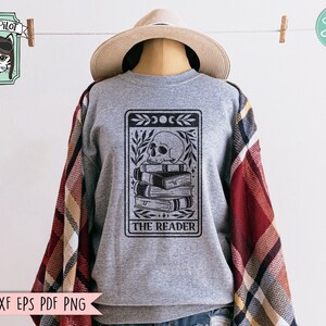 May include: Gray sweatshirt with a black and white illustration of a skull with a stack of books and the text "THE READER" on a tarot card design.