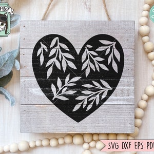May include: A black heart shape with white leafy branches inside. The heart is on a light gray wooden background.