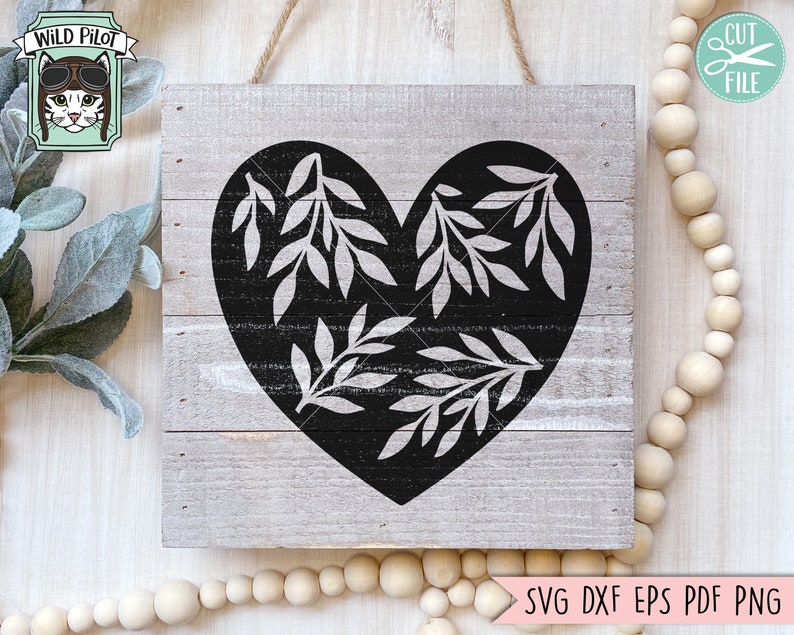 May include: A black heart shape with white leafy branches inside. The heart is on a light gray wooden background.
