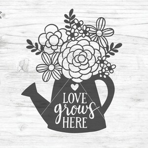 May include: Black and white silhouette of a watering can with flowers and the text "LOVE grows HERE" on a white wood background.
