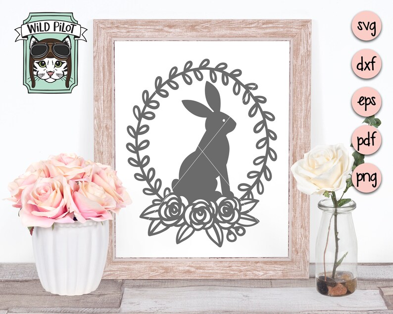 May include: A gray bunny rabbit silhouette inside a wreath of leaves with three roses at the bottom. The image is in a wooden frame with a white background.